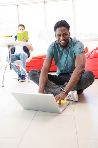 Smiling young man using laptop on floor