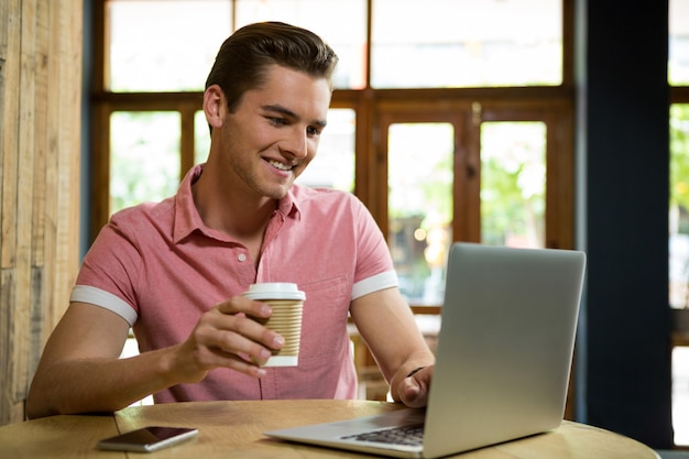 カフェでコーヒーを飲みながらノートパソコンを使用して笑顔の若い男