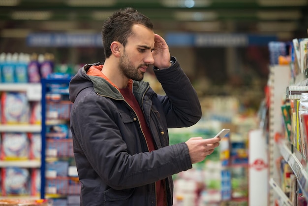 smiling young man using mobile phone while shopping in shopping store