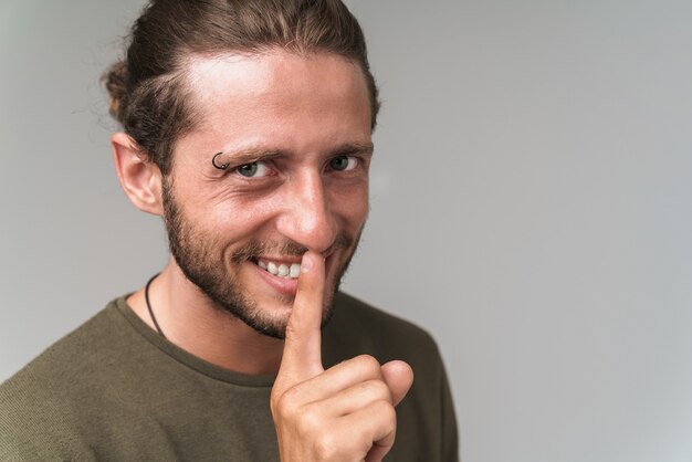 Smiling young man wearing casual outfit showing silence gesture isolated gray