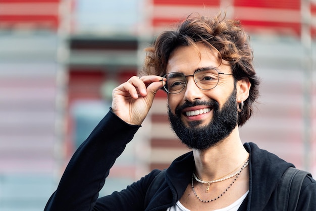 Smiling young man with beard putting on glasses