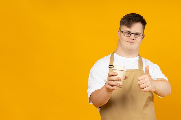 A smiling young man with cerebral palsy in glasses as a barista in an apron and with coffee World Genetic Diseases Day concept place for text