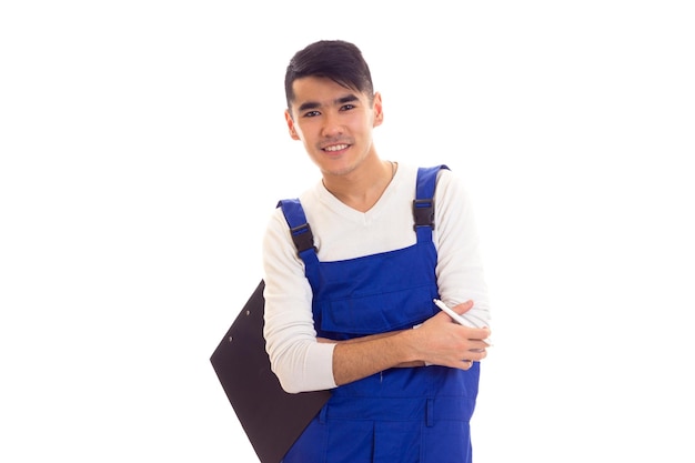 Smiling young man with dark hair wearing in shirt and overall holding white pen and black folder