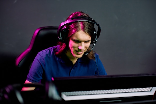 Photo smiling young man with long hair playing network game while talking to game ally via hands-free headset with microphone
