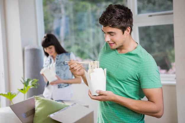 Smiling young man and woman eating noodles at home