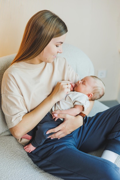 A smiling young mother is sitting on a sofa and holding a newborn baby in her arms A happy mother with a child in her arms The concept of motherhood