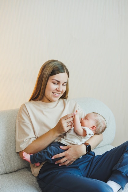 A smiling young mother is sitting on a sofa and holding a newborn baby in her arms A happy mother with a child in her arms The concept of motherhood