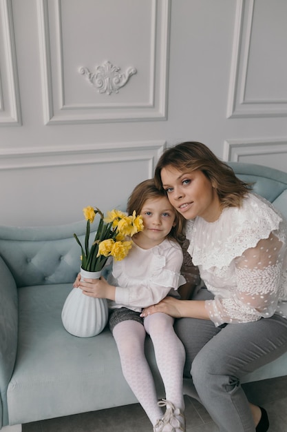 Smiling young mother and little daughter cuddle have fun sitting on couch at home overjoyed mom or nanny playing with small preschooler girl child tickle and laugh enjoy leisure weekend at home