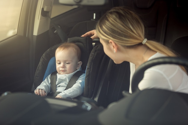 Smiling young mother looking at her child sitting in safety seat