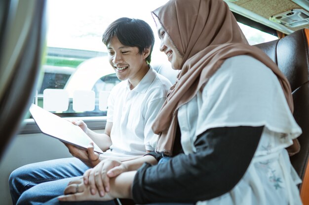 A smiling young Muslim couple looking at the screen of a tablet together while sitting on the bus