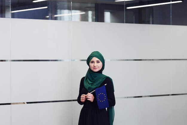 Smiling young muslim woman in scarf with european flag in
hands