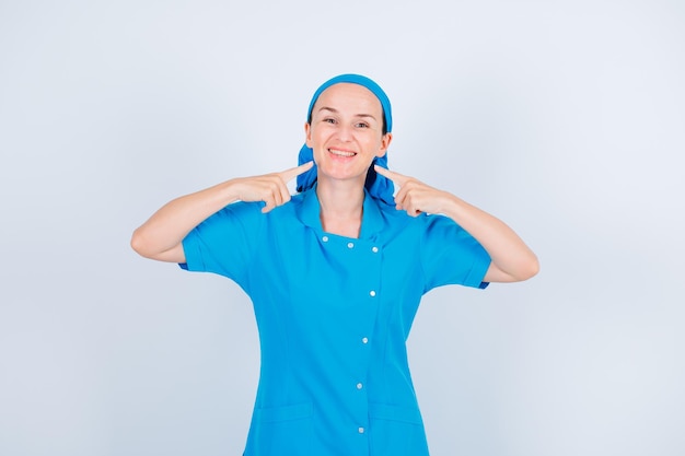 Smiling young nurse is showing her smile with forefingers on white background