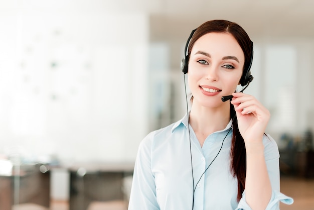 Giovane impiegato di concetto sorridente con una cuffia avricolare che risponde in un call center, donna che parla con i clienti. ritratto di un cliente attraente e rappresentante del supporto tecnico