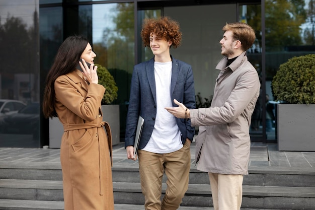 Giovani sorridenti ragazza e uomini comunicano vicino all'ufficio moderno all'aperto ragazza che parla sullo smartphone