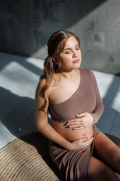 Photo smiling young pregnant woman in top and skirt posing in studio and stroking her belly pregnant pregnant woman happy pregnancy