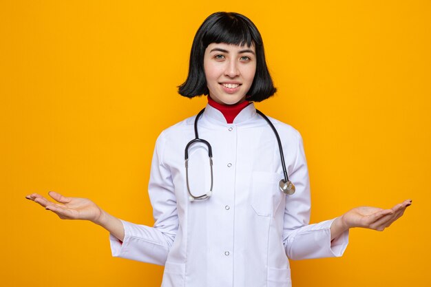 Sorridente giovane bella ragazza caucasica in uniforme da medico con stetoscopio che si tiene per mano aperta