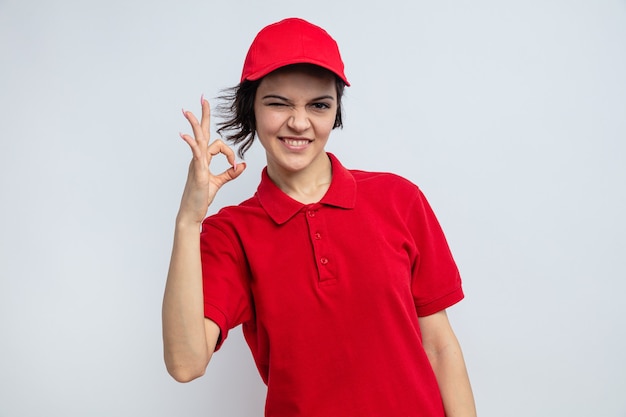 Smiling young pretty delivery woman blinks her eye and gestures ok sign