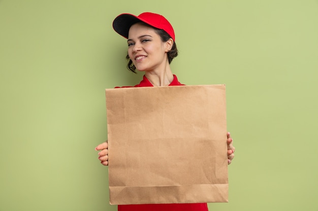 Smiling young pretty delivery woman holding paper food packaging and 