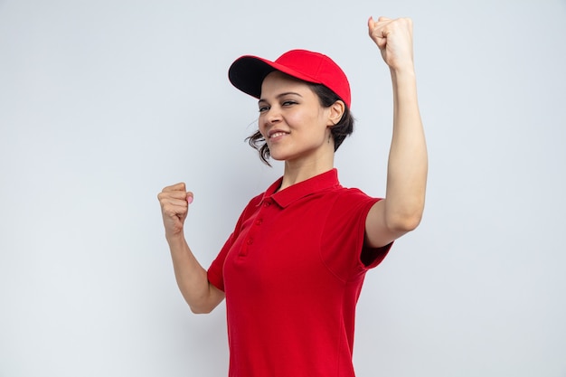 Smiling young pretty delivery woman standing with raised fists 