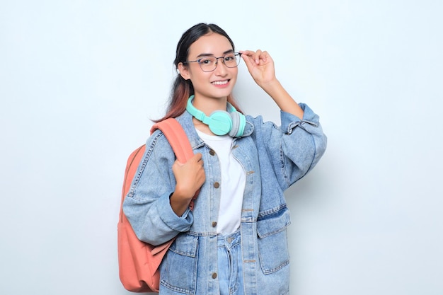 Smiling young pretty woman wearing a backpack touching eyeglasses isolated on white background