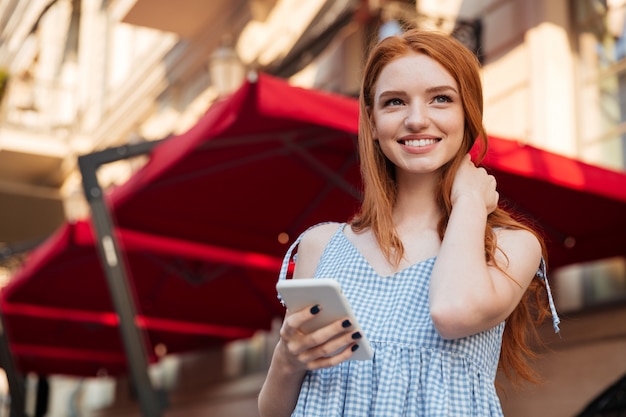 Smiling young redhead woman holding mobile phone