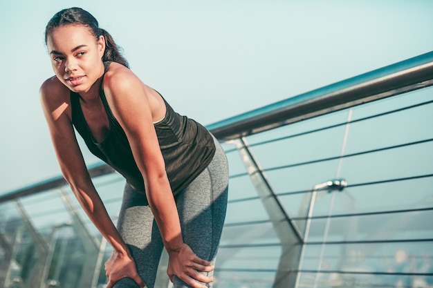 Smiling young sportswoman standing on the bridge with hands on the laps