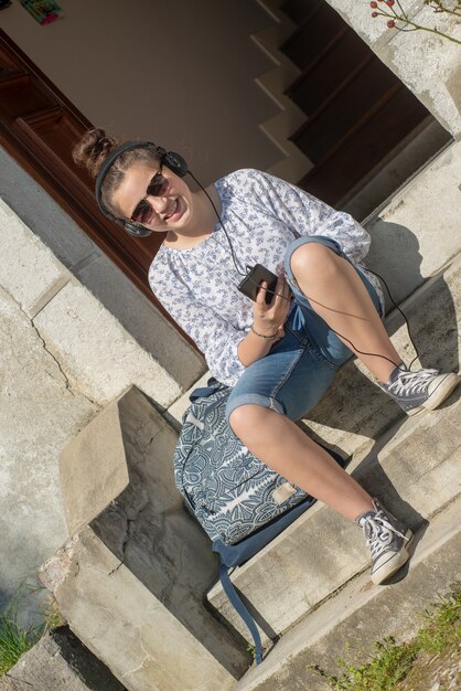 Smiling young teen girl sitting on the steps, listening a music