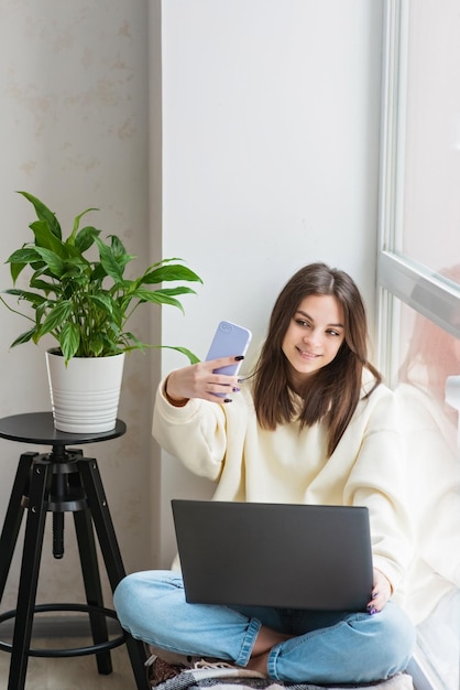 Smiling young teenage girl video calling on mobile phone talking to friend family taking selfie for social media staying connected during pandemic Soft selective focus