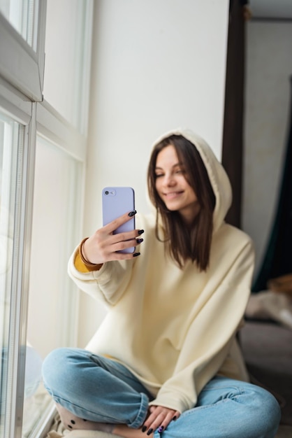 Smiling young teenage girl video calling on mobile phone talking to friend family taking selfie for social media staying connected during pandemic Soft selective focus