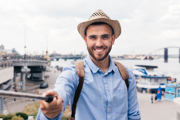 Smiling young traveler wearing hat and taking selfie at outdoors