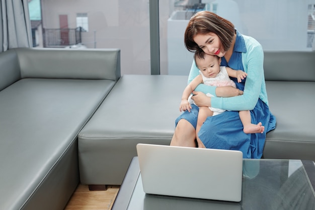 Smiling young Vietnamese woman with baby on laps video calling her relative, friend or doctor