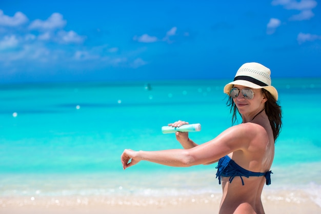 Улыбается молодая женщина, применяя солнцезащитный крем на пляже