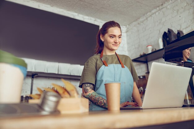 Smiling young woman barista using notebook in coffee shop