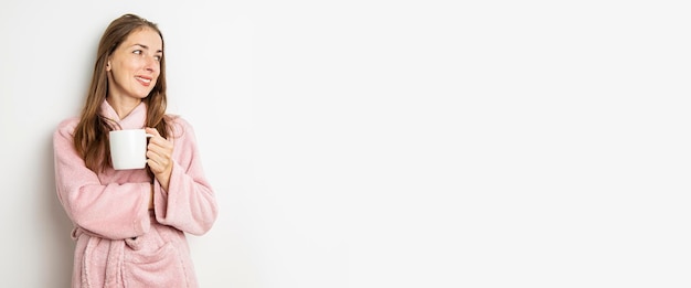 Smiling young woman in a bathrobe with a cup on a white background Banner