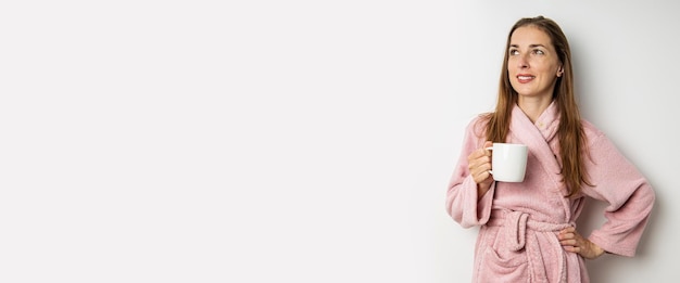 Smiling young woman in a bathrobe with a cup on a white background Banner