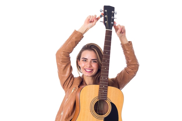 Foto giovane donna sorridente in giacca marrone con la chitarra che si tiene per mano su sfondo bianco in studio