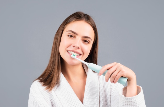 웃고 있는 젊은 여성이 아침에 치아를 청소하는 미백 치약이 포함된 칫솔을 사용하여 이를 닦고 있습니다 치약이 포함된 칫솔