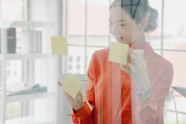 Photo smiling young woman by adhesive notes seen through glass window