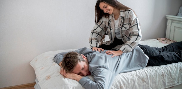 A smiling young woman in casual clothing is giving a playful back massage