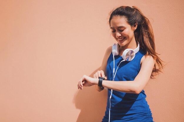 Smiling young woman checking the time while standing against wall