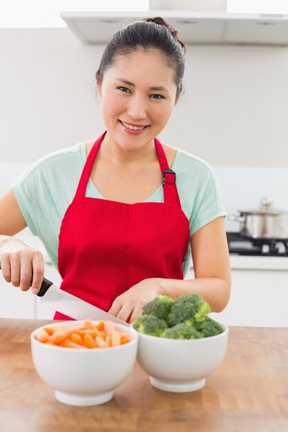 Foto giovane donna sorridente che taglia le verdure a pezzi in cucina