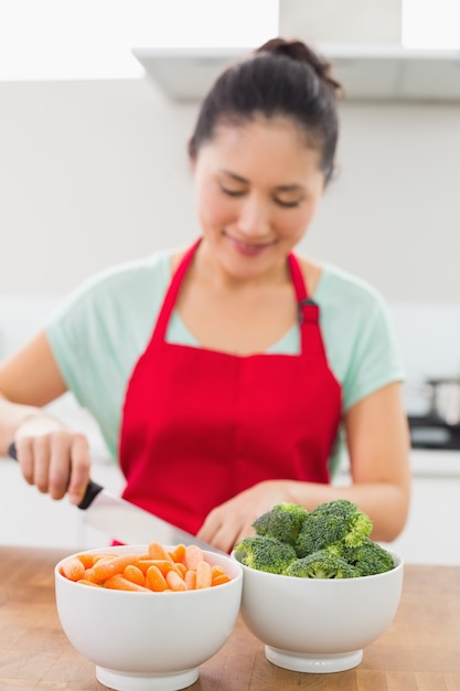 Smiling young woman chopping vegetables in kitchen