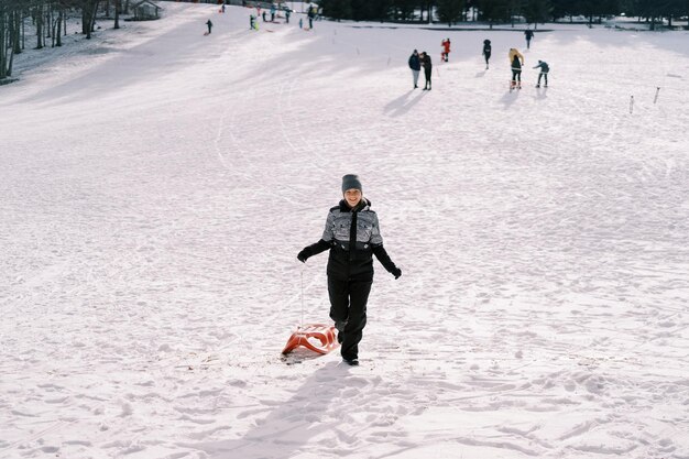 Smiling young woman climbing a hill with a sled in her hands