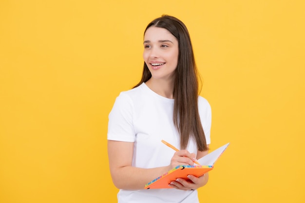 고립 된 노란색 배경에 책을 들고 웃는 젊은 여자 대학생 얼굴 표정을 감정적으로 보여주는 모델 메모를 작성 잠겨있는 어린 소녀의 초상화