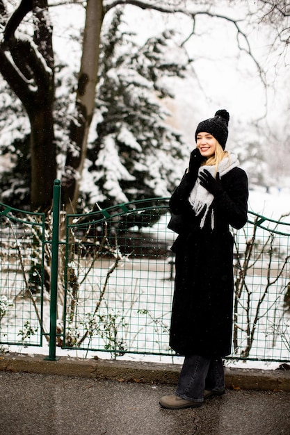 Sorridente giovane donna in abbigliamento accogliente utilizzando il telefono cellulare e tenendo la tazza di caffè il giorno d'inverno