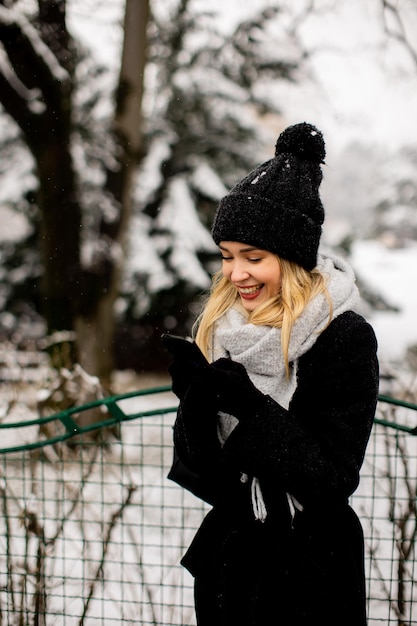 Smiling Young Woman in Cozy Clothing using mobile phone on winter day