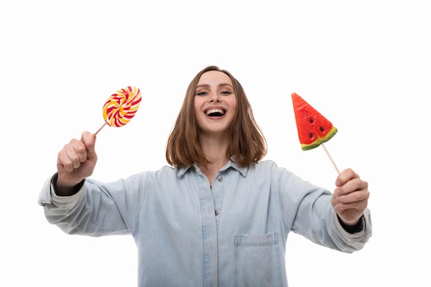 Photo a smiling young woman in a denim shirt poses with colored lollipops on a white background