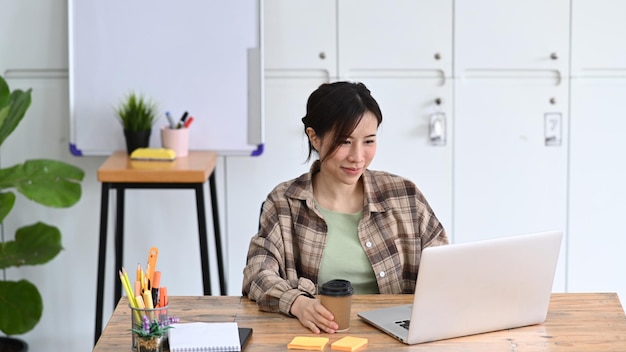 현대 직장에서 노트북으로 일하는 웃고 있는 젊은 여성 디자이너
