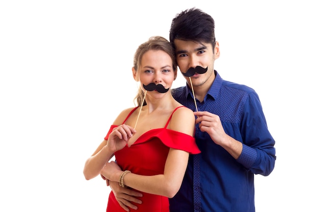 Smiling young woman in dress and young handsome man in shirt holding cardboard sticks of moustaches