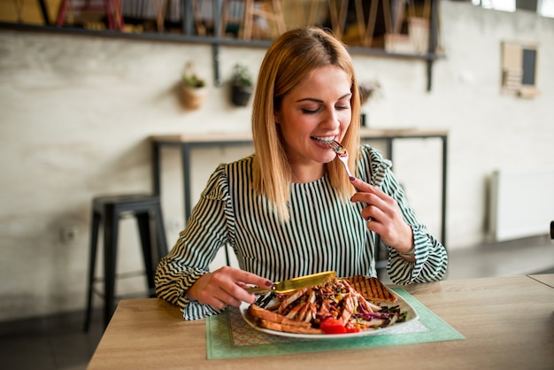 Smiling young woman eating lunch in restaurant.